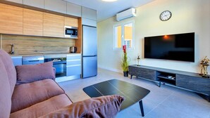 A modern living room with a sofa, a flat-screen TV, and a kitchen area with a microwave and refrigerator. - 1bedroom ocean view apartment (Costa Adeje)