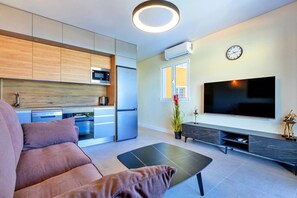 Ein modernes Wohnzimmer mit einer Couch, einem Flachbildfernseher und einer Küchenzeile mit Mikrowelle und Kühlschrank.