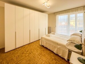 A bedroom with a large wardrobe, a bed with a white bedspread, and a window with a view of buildings. - La Maison del Borgo - Bergamo (Bergamo)