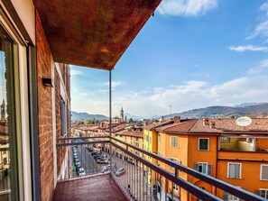A balcony with a view of a street lined with colorful buildings, a clear sky, and distant hills. - La Maison del Borgo - Bergamo (Bergamo)