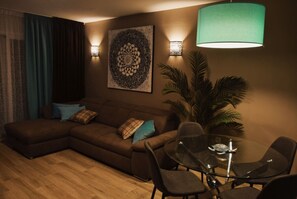 A living room with a sectional sofa, a glass coffee table, and a dining area with chairs. - Ocean-View Apartment with Pool in Los Gigantes (Torviscas Bajo)