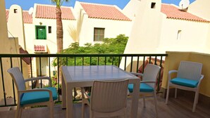 Un balcón con mobiliario de mimbre y una mesa, con vistas a una zona residencial de tejados rojos.