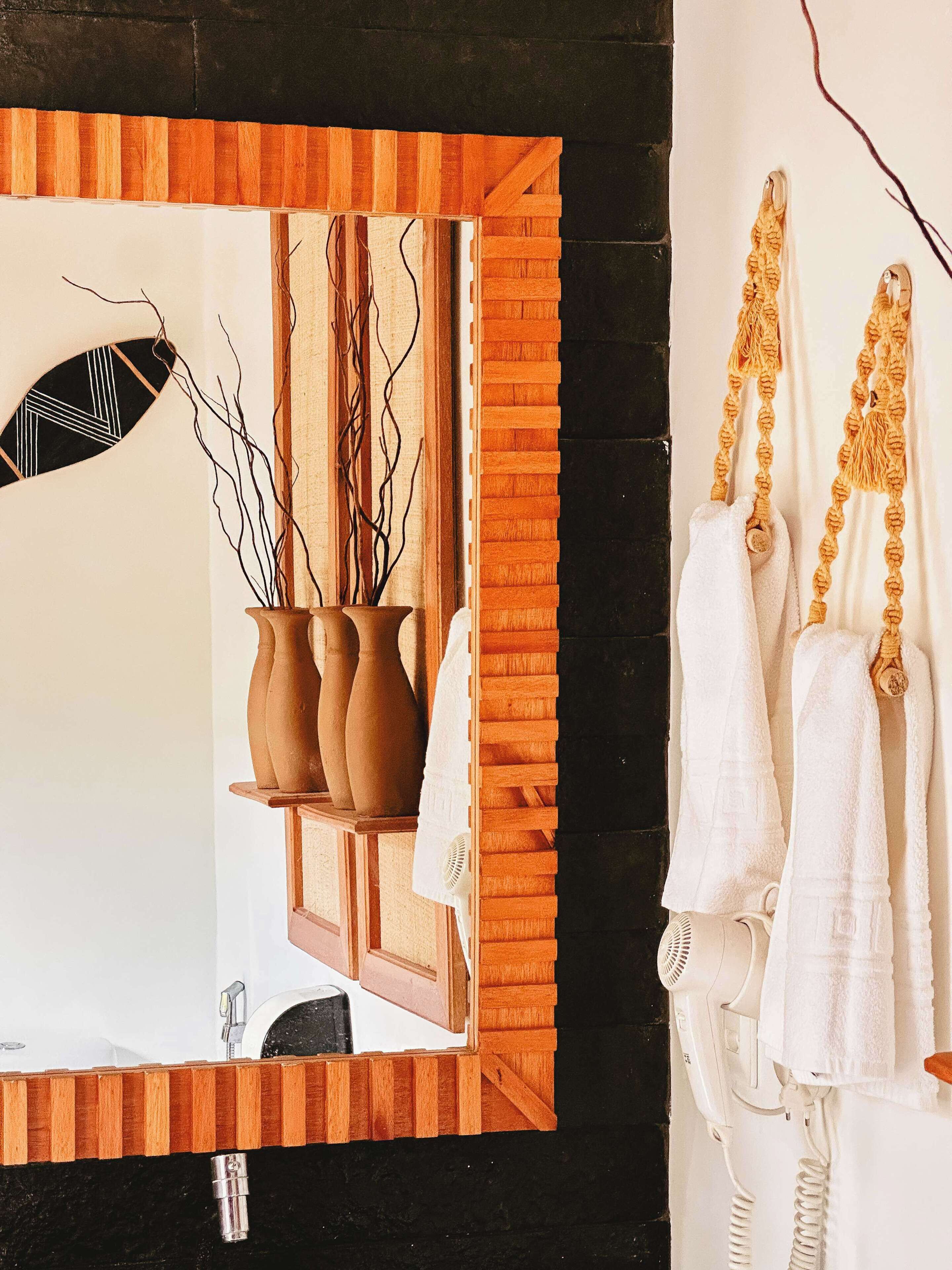 Un bagno con un mobile vanitario in legno, uno specchio con cornice geometrica e un porta asciugamani con asciugamani bianchi.