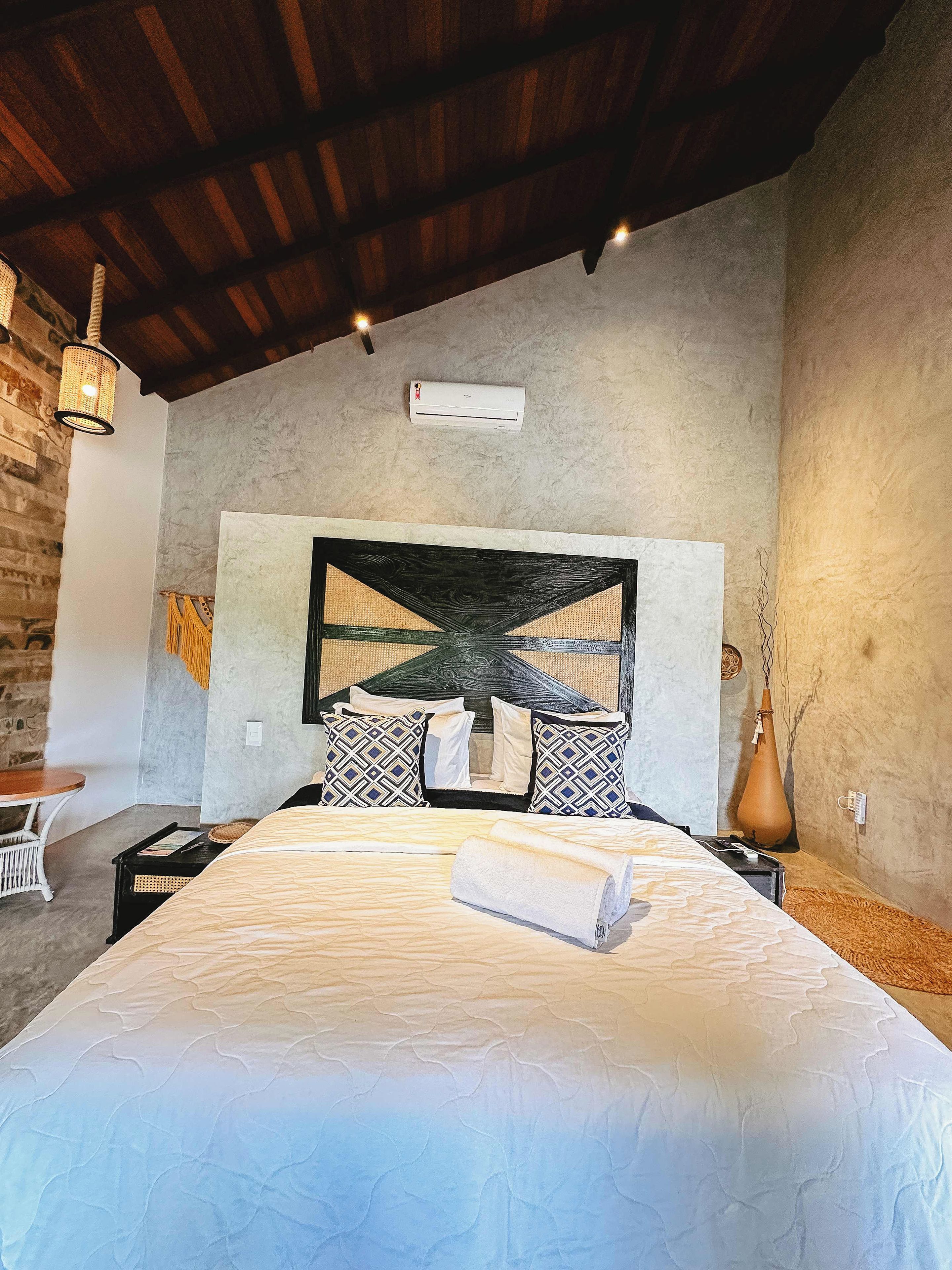 A bedroom with a bed, a headboard, a wall-mounted air conditioner, and a hanging light fixture.