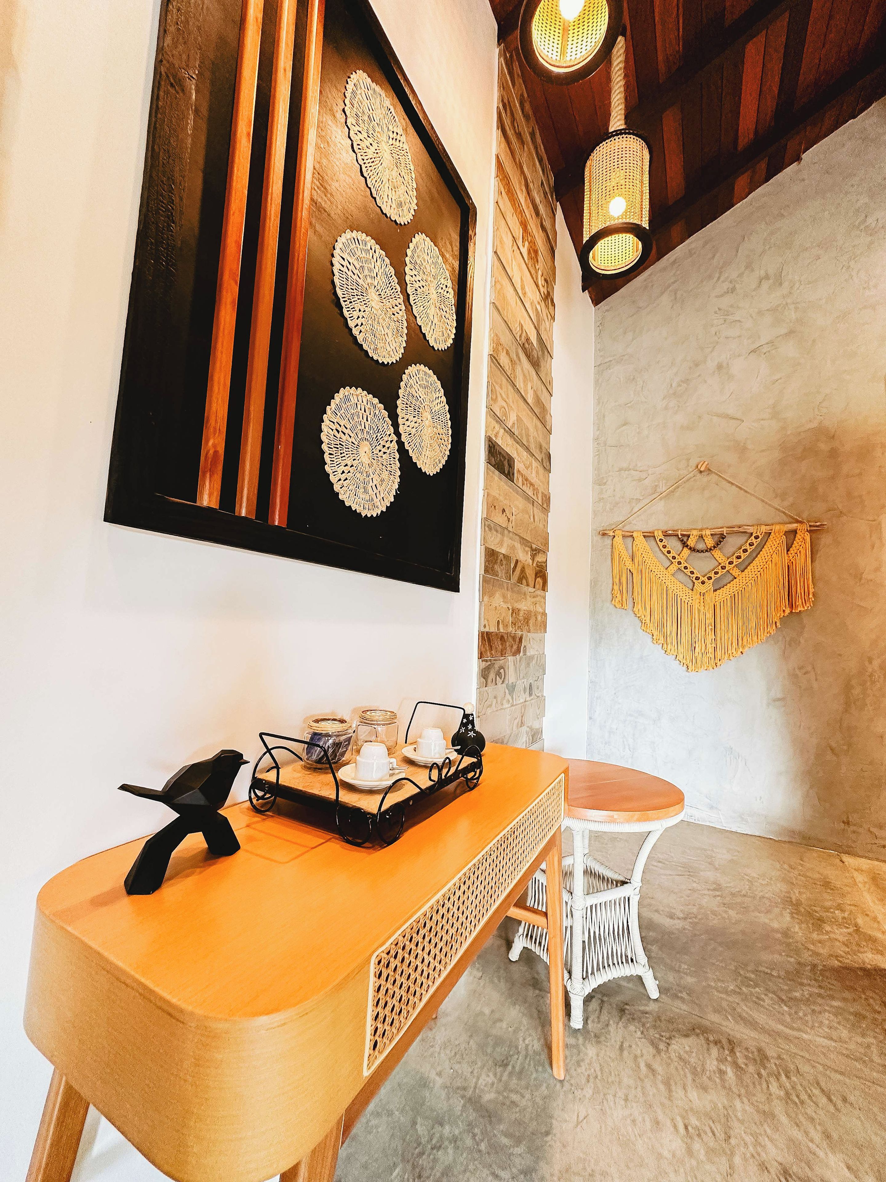 A wooden table with a tray of items, a hanging macrame wall decoration, and a framed artwork with geometric patterns.
