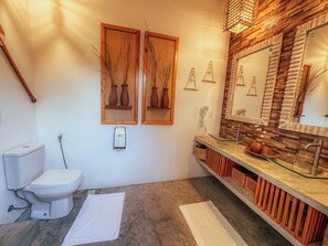 A bathroom with a toilet, bidet, and a vanity with a glass sink and wooden vanity. - Quarto triplo beira mar (Cruz)