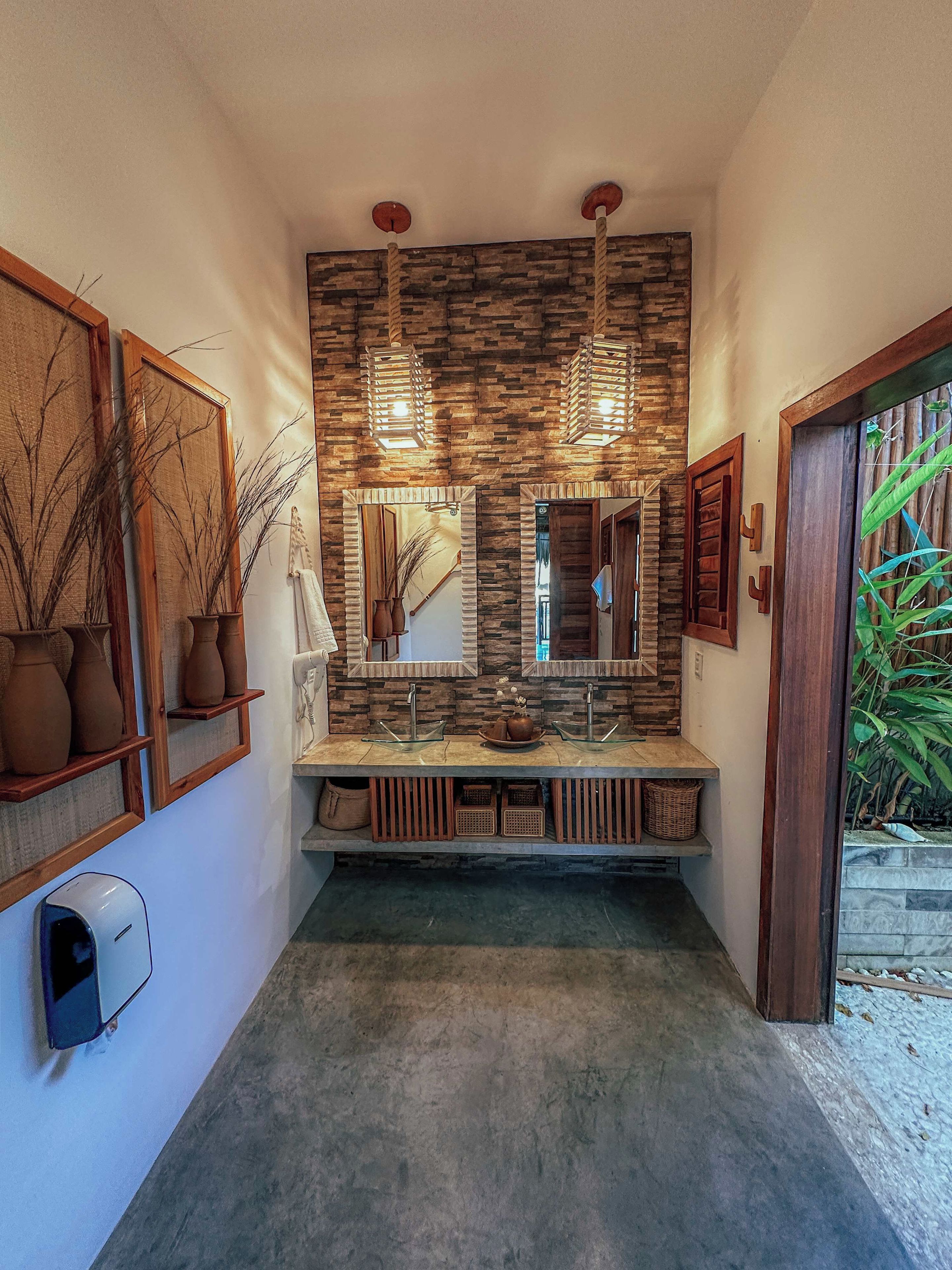 A bathroom with a stone wall, two mirrors, a sink, and a hand dryer.