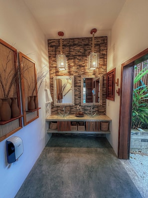 A bathroom with a stone wall, two mirrors, a sink, and a hand dryer. - Quarto triplo beira mar (Cruz)