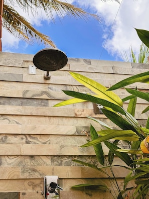 A stone wall with a solar panel and a water spout. - Quarto triplo beira mar (Cruz)