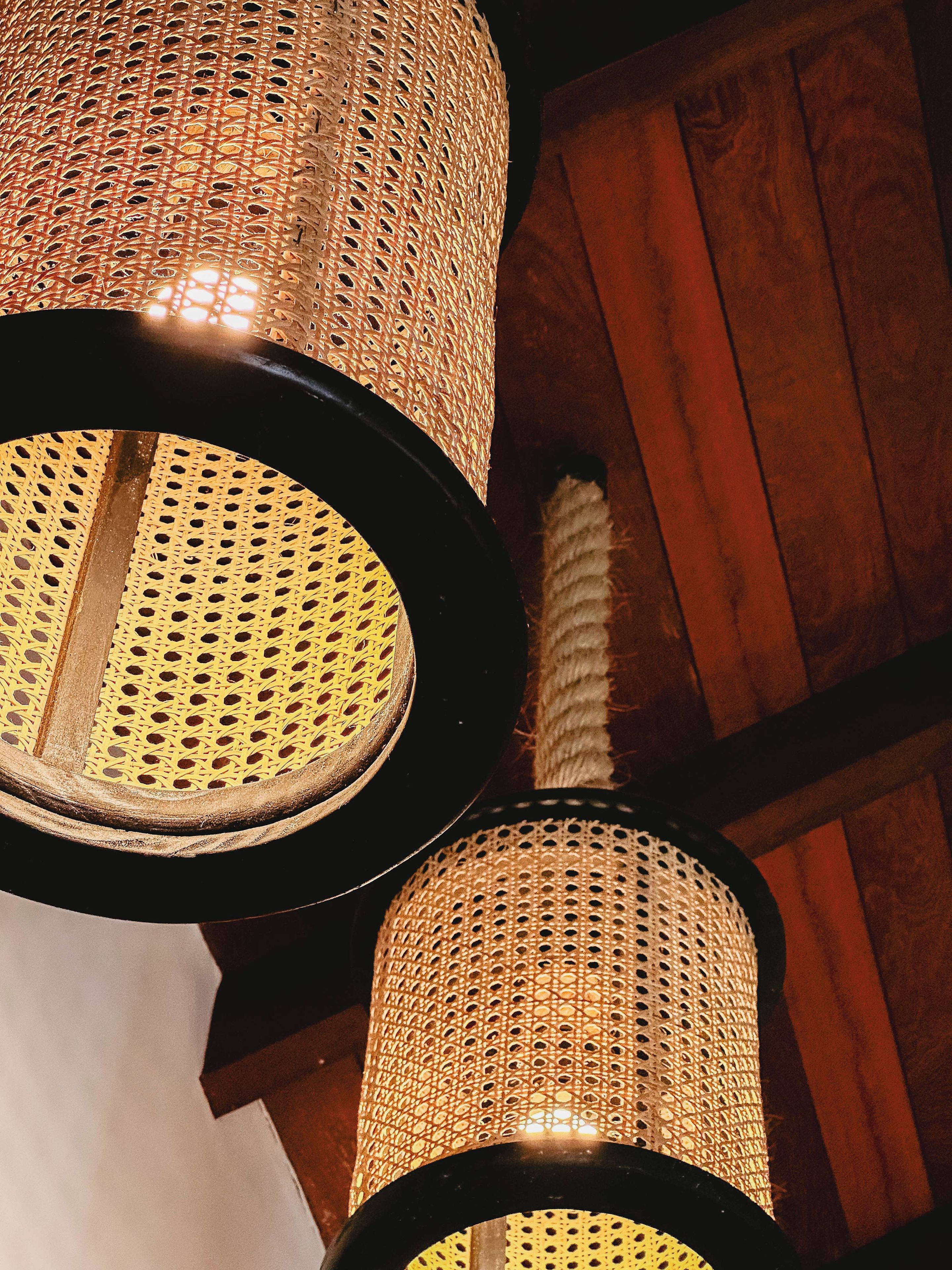 Gros plan de lampes dont les abat-jour sont faits d’un tissu tissé en forme de cylindre, avec une tige centrale, le tout sur un fond en bois.