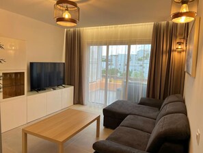 Ein modernes Wohnzimmer mit Flachbildfernseher, Couchtisch aus Holz und einer Couch.