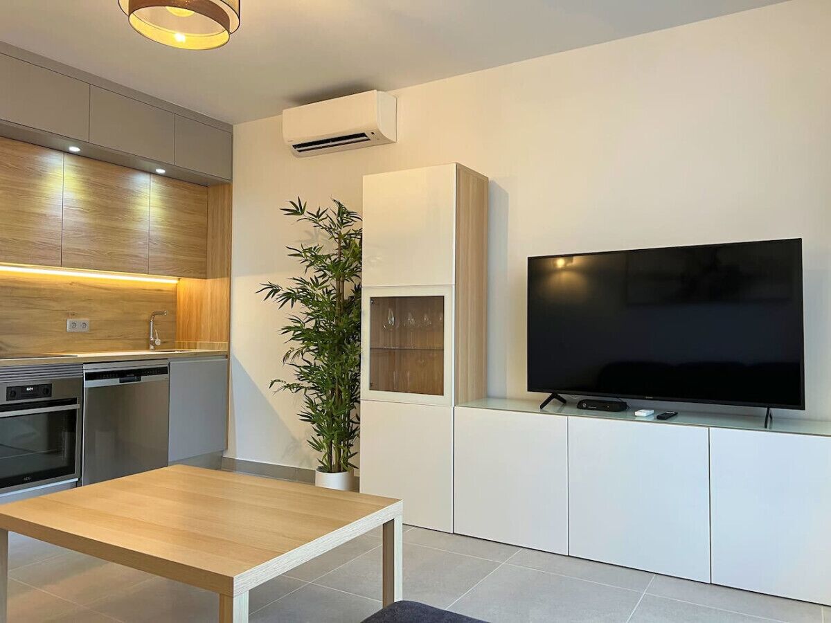 Cozinha moderna com eletrodomésticos embutidos, espaço de refeições com mesa e televisão de tela plana fixada em um armário branco.