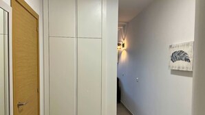 En hall med en dörr av trä, en vit garderob och en väggmonterad lampa.