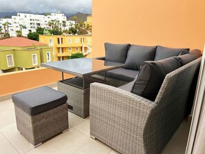 A balcony with wicker furniture, including a sofa and ottoman, and a view of buildings in the background. - Orlando apartment with views (Costa Adeje)