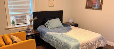 A bedroom with a bed, a nightstand, a chair, a window with blinds, and wall decorations.