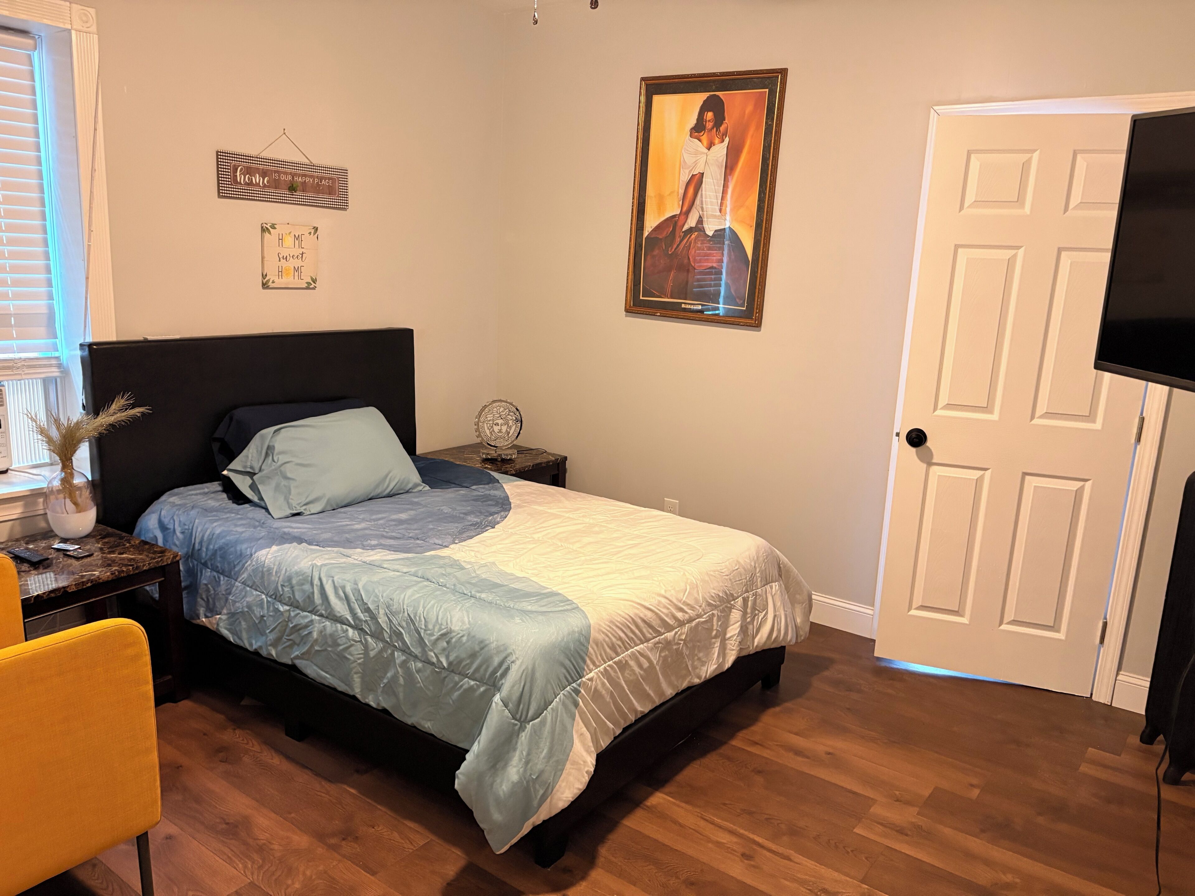 A bedroom with a bed, bedside tables, a chair, a door, and a wall-mounted TV.
