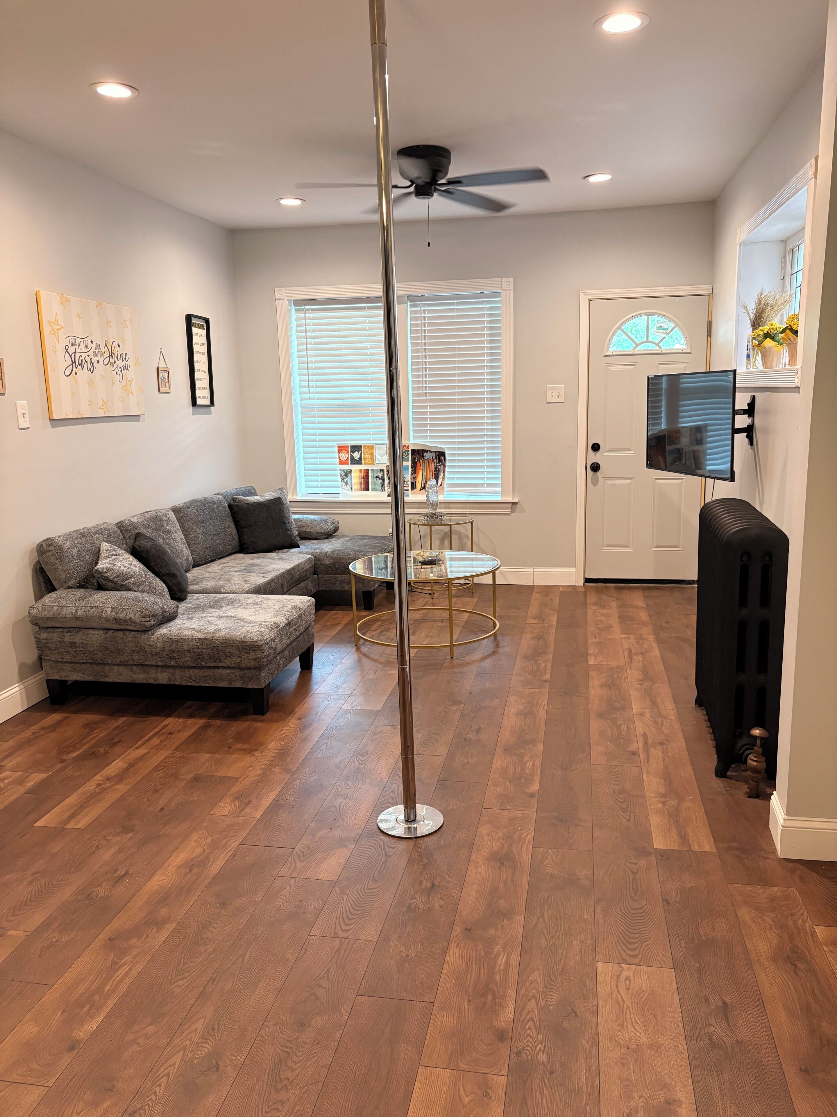 A living room with a sectional sofa, a glass-top coffee table, a ceiling fan, and a door leading to another room.