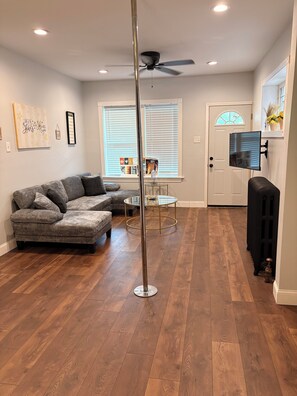 A living room with a sectional sofa, a glass-top coffee table, a ceiling fan, and a door leading to another room.