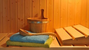 Eine Holzsauna mit einem Holzeimer, einem Holzkellen und einem Stapel Handtücher.