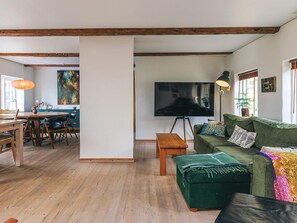 Ein geräumiges Wohnzimmer mit Holzboden, einem grünen Sofa, einem Couchtisch und einem Fernseher auf einem Dreibeinstativ.
