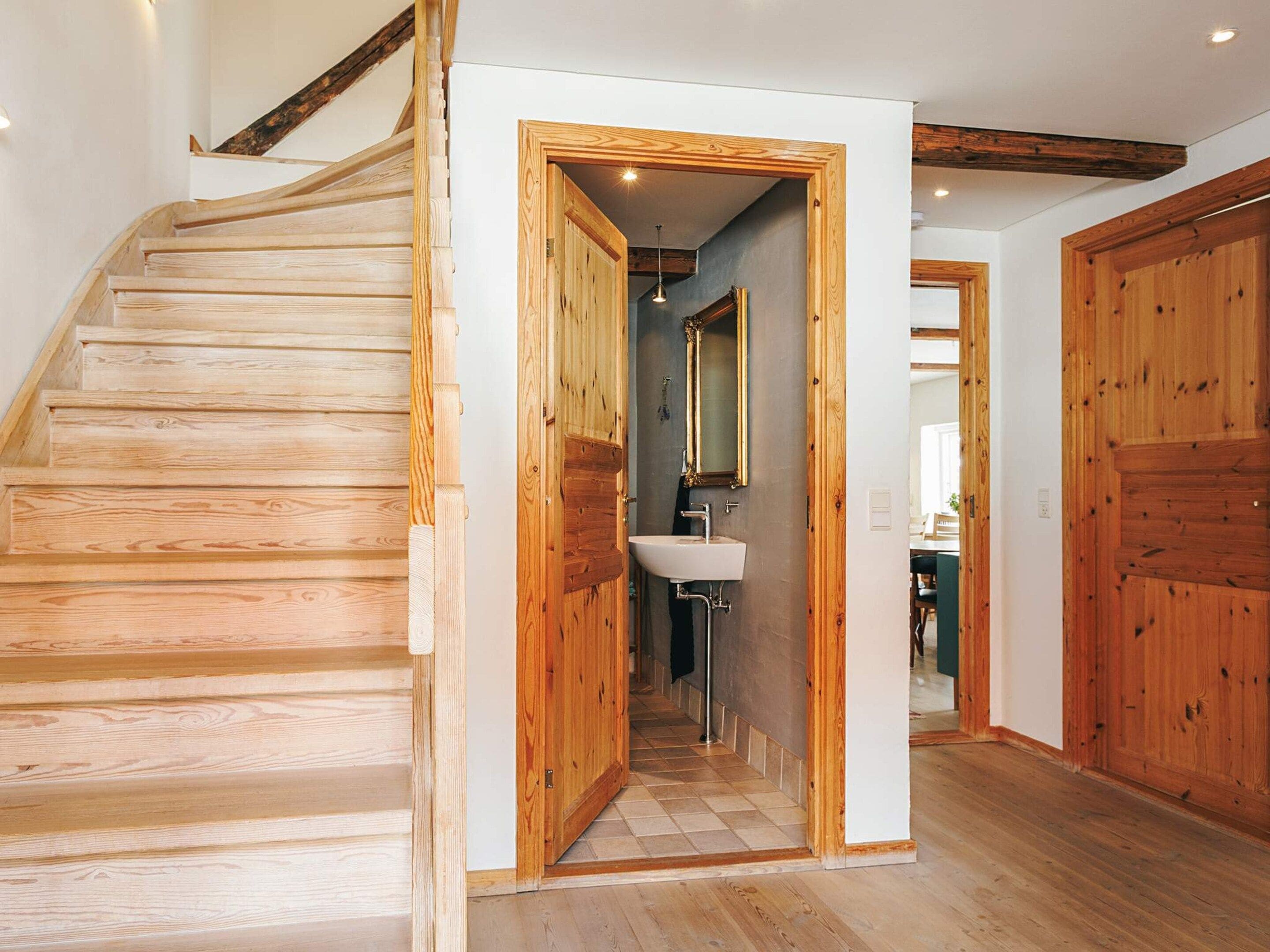Eine Holztreppe führt zu einem Badezimmer mit Waschbecken und Spiegel.