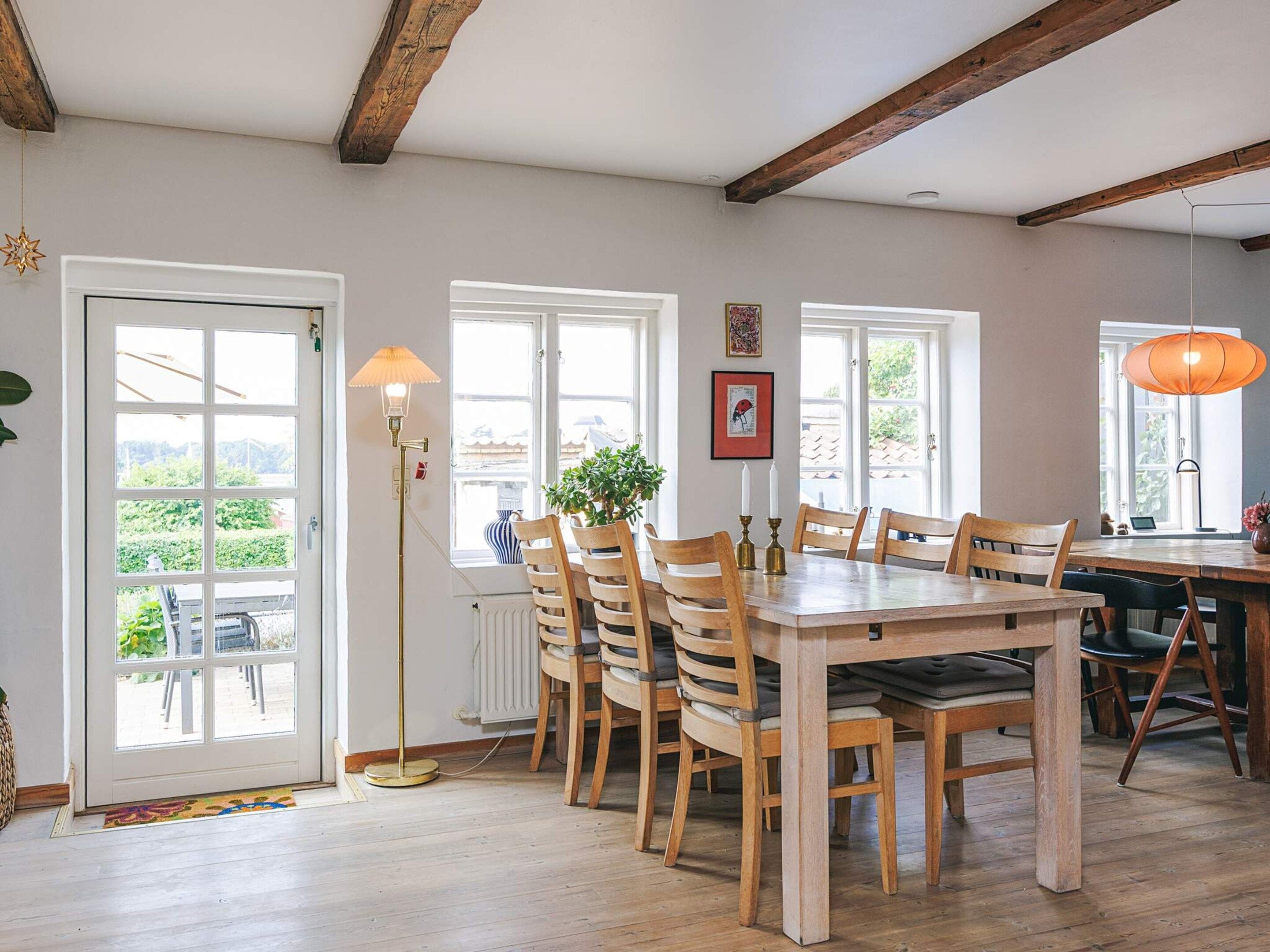A dining area with a wooden table and chairs, a floor lamp, and a view through a window.
