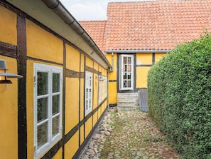 Ein gelbes Gebäude mit einem Ziegeldach, einem schmalen Pfad und einer Hecke.
