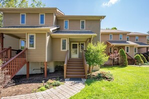 A two-story residential building with a covered porch, a staircase leading to the entrance, and a well-maintained lawn. - New! Lake Area Townhome w/ Hot Tub (McHenry)