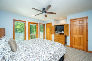 A bedroom with a bed, a ceiling fan, a TV, wooden cabinets, and a large door. - New! Lake Area Townhome w/ Hot Tub (McHenry)