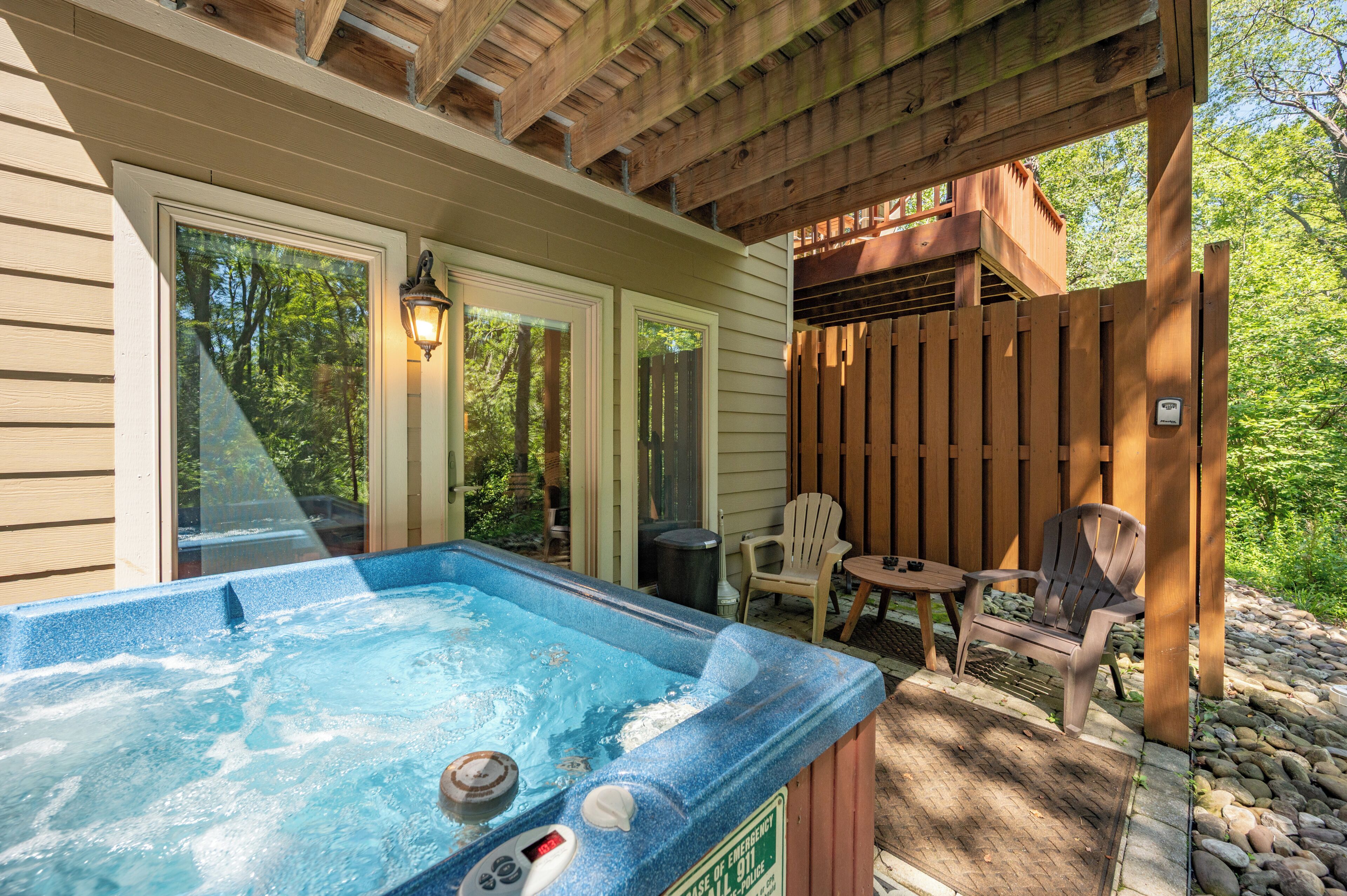A hot tub area with a wooden deck, outdoor seating, and a view of the surrounding greenery.