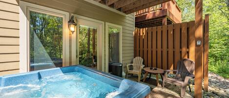 A hot tub area with a wooden deck, outdoor seating, and a view of the surrounding greenery.