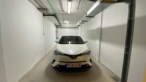 A white car parked in a narrow, well-lit hallway with white walls and visible pipes. - Ocean-View Apartment with Pool in Los Gigantes (Santiago del Teide)