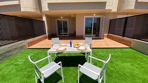 An outdoor patio with a table set for two, surrounded by artificial grass, and enclosed by a black fence. - Ocean-View Apartment with Pool in Los Gigantes (Santiago del Teide)