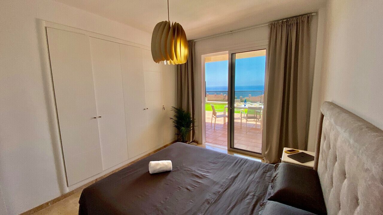 A hotel room with a bed, a large window with curtains, a view of the outdoors, and a ceiling light.