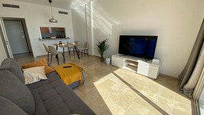 A modern living room with a sofa, a TV, a dining area, and a kitchen in the background. - Ocean-View Apartment with Pool in Los Gigantes (Santiago del Teide)