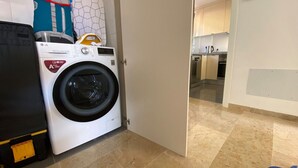A laundry area with a front-loading washing machine, a dryer, and a kitchen visible in the background. - Ocean-View Apartment with Pool in Los Gigantes (Santiago del Teide)