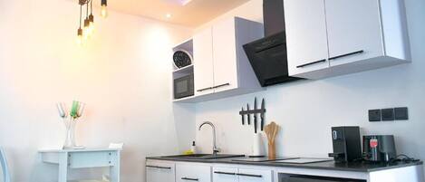 A modern kitchen with white cabinets, a built-in microwave, and a coffee machine.