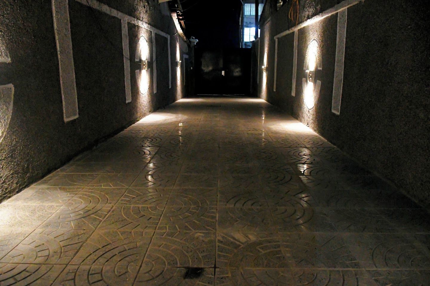 A corridor with patterned flooring and wall-mounted lights.