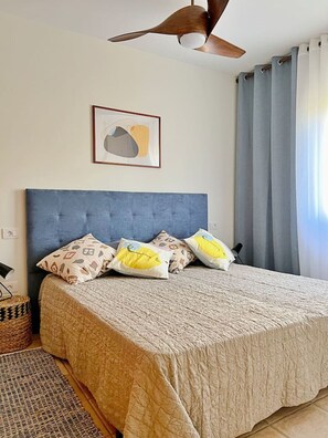 Ein Schlafzimmer mit einem Bett, einem Deckenventilator, einem gerahmten abstrakten Gemälde und einem Fenster mit Vorhängen.