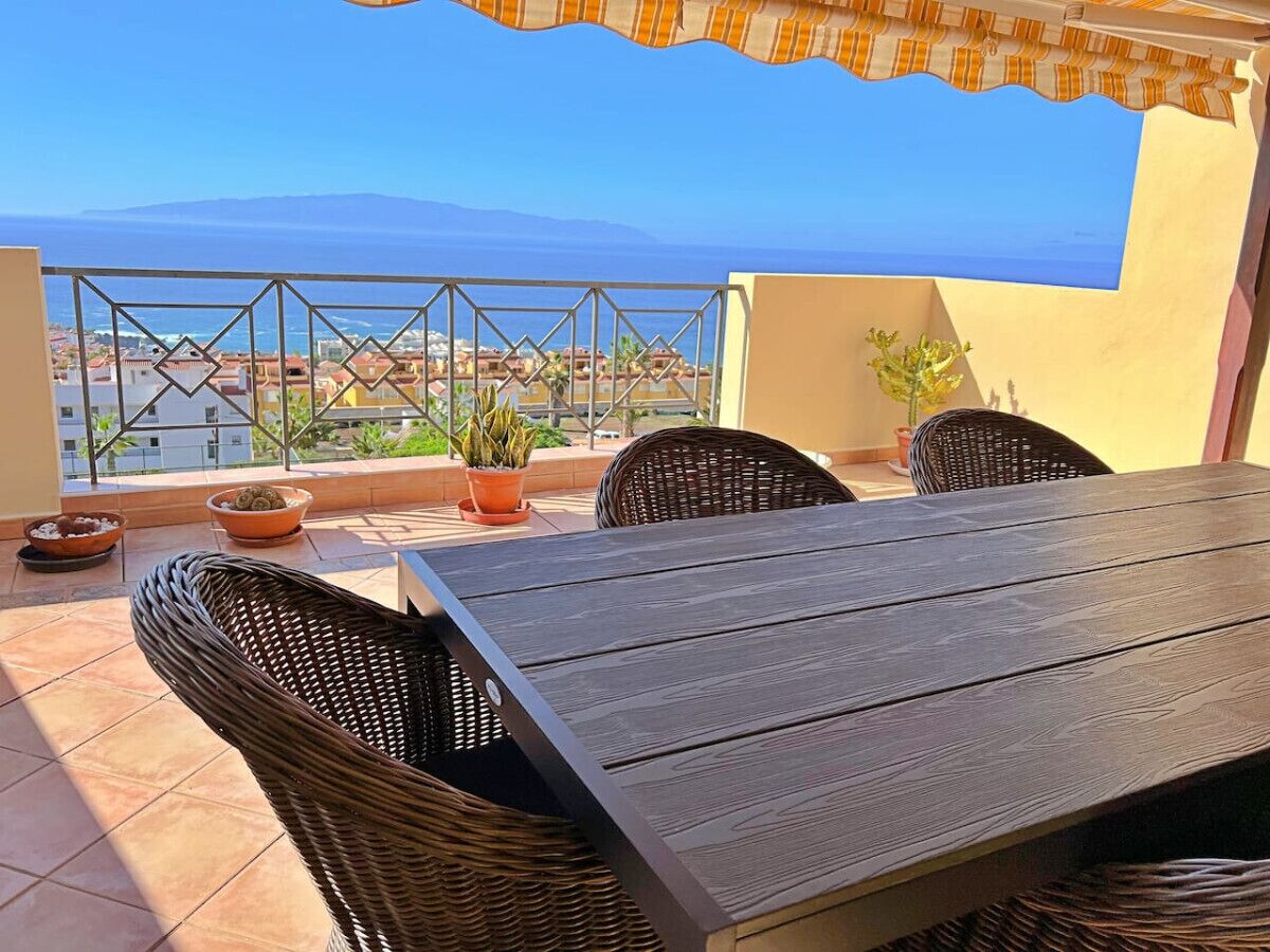 Une terrasse avec une table et des chaises, des plantes en pot et une vue sur la mer et les bâtiments.