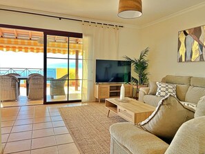 A living room with a television, sofa, and a view of the outdoors through a glass door. - Amazing view apartment (Santiago del Teide)