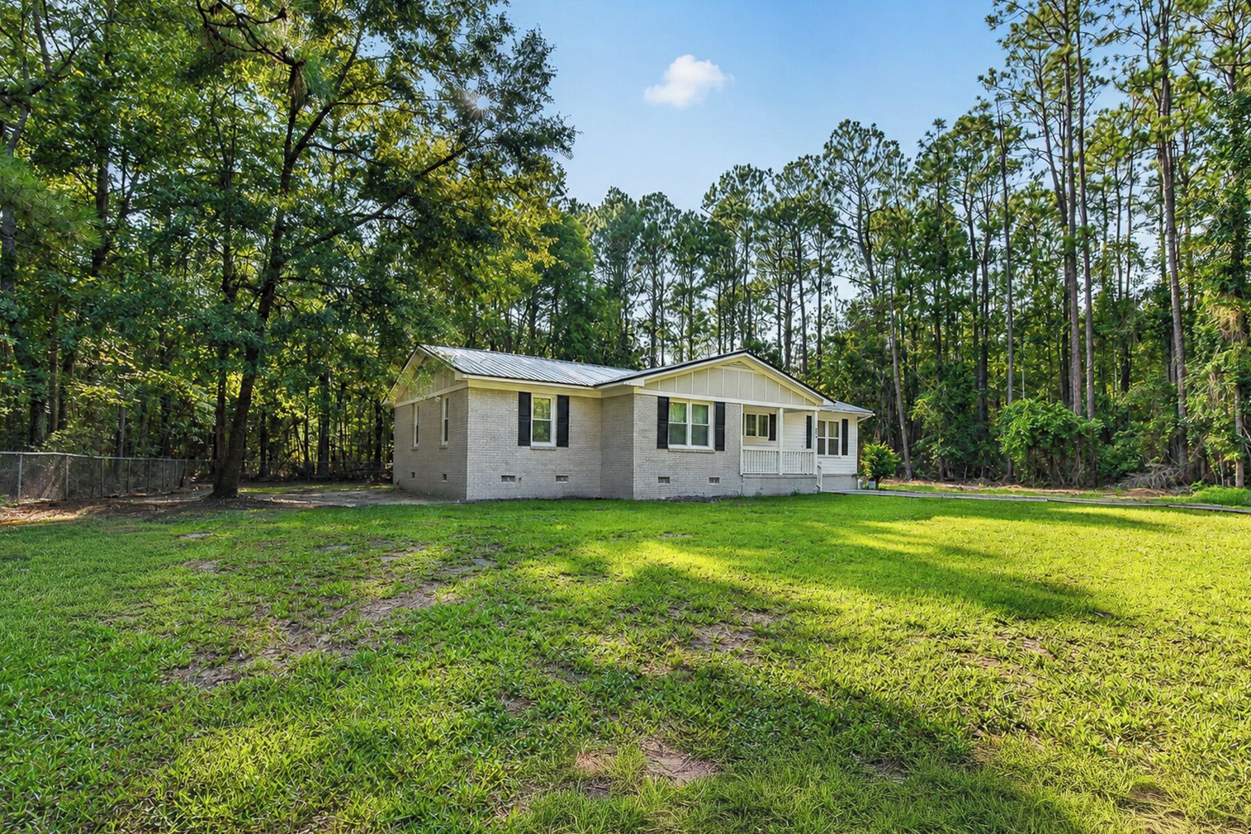 A single-story house with a gabled roof, surrounded by a grassy yard and tall trees.