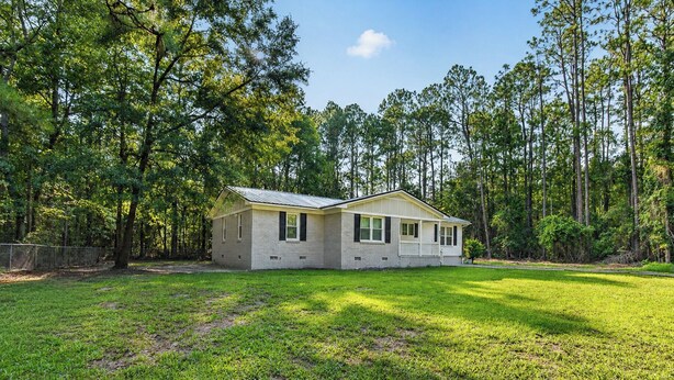 A single-story house with a gabled roof, surrounded by a grassy yard and tall trees.