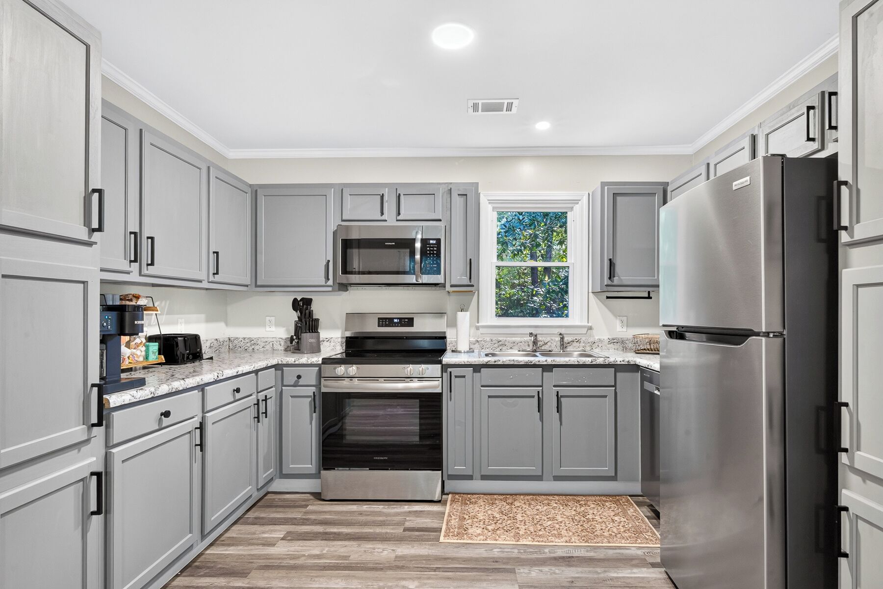 A modern kitchen with grey cabinetry, stainless steel appliances, and a window with a view of greenery.