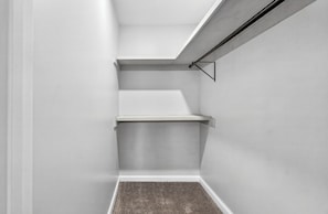 Un cantó d'una habitació amb parets blanques, una catifes grisa i una làmpada al sostre negra.