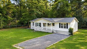 A single-story house with a front porch, a gravel driveway, and a fenced yard.