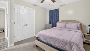 A bedroom with a bed, a ceiling fan, a door, and a window with curtains.