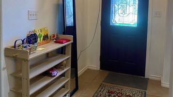 Een gang met een houten schoenenrek, een wandlamp, een deur met een glas-in-loodraam en een kamerbreed tapijt.