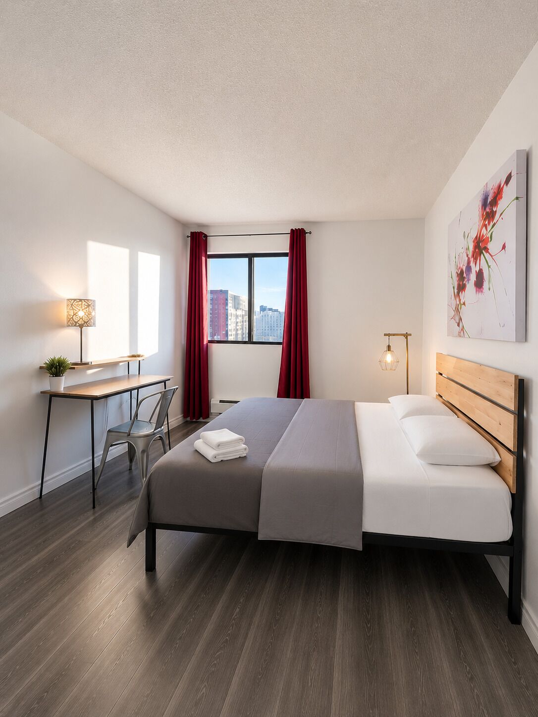 Quarto de hotel moderno com cama, escrivaninha, cadeira e vista da cidade através de uma janela com cortinas vermelhas.