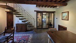 A spacious room with a wooden staircase, a dining table, and a view into another room. - Villa Tufi by MMega (Montone)
